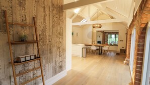 Une cuisine spacieuse avec une échelle en bois adossée à un mur rustique, un coin repas avec une grande table et des chaises, et une vue sur l’extérieur par une fenêtre.