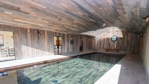 Une grande piscine intérieure avec un plafond et des murs en bois, un banc le long du bord et une horloge au mur.