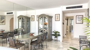 A dining area with a glass table, metal chairs, and a large mirror. There are two ornate wooden cabinets and a potted plant.