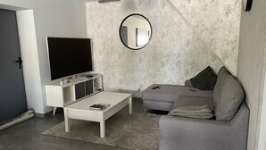 A modern living room with a white TV stand, grey sofa, and a round mirror on the wall.