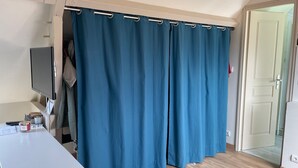 A room with a large blue curtain, a flat-screen TV, a small table with various items, and a wooden floor.