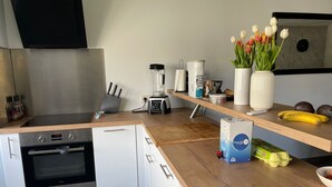 A modern kitchen with white cabinets, a built-in oven, a coffee maker, a blender, and a fruit bowl.