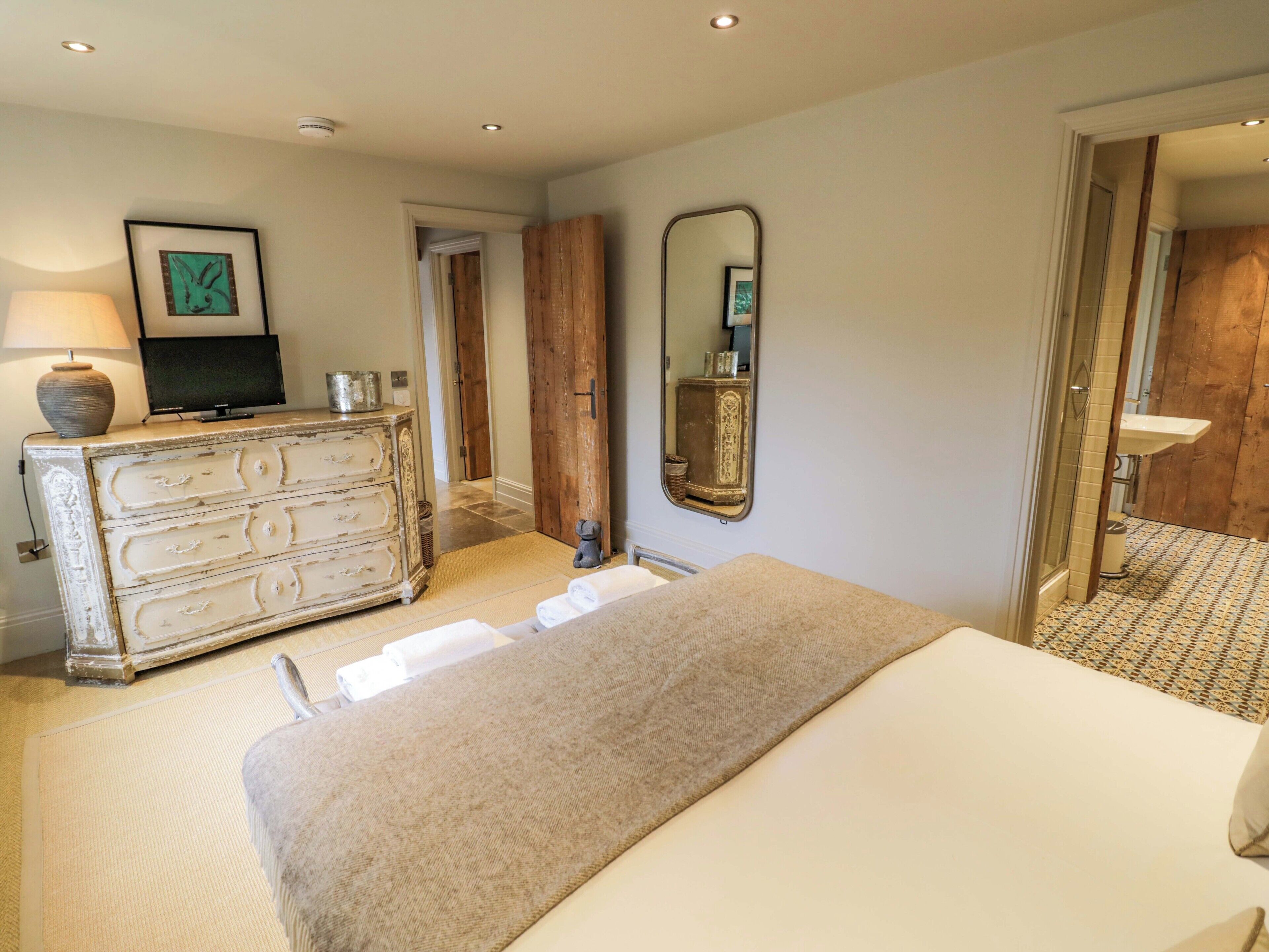 A bedroom with a bed, a dresser, a mirror, a television, and a bathroom visible through an open door.