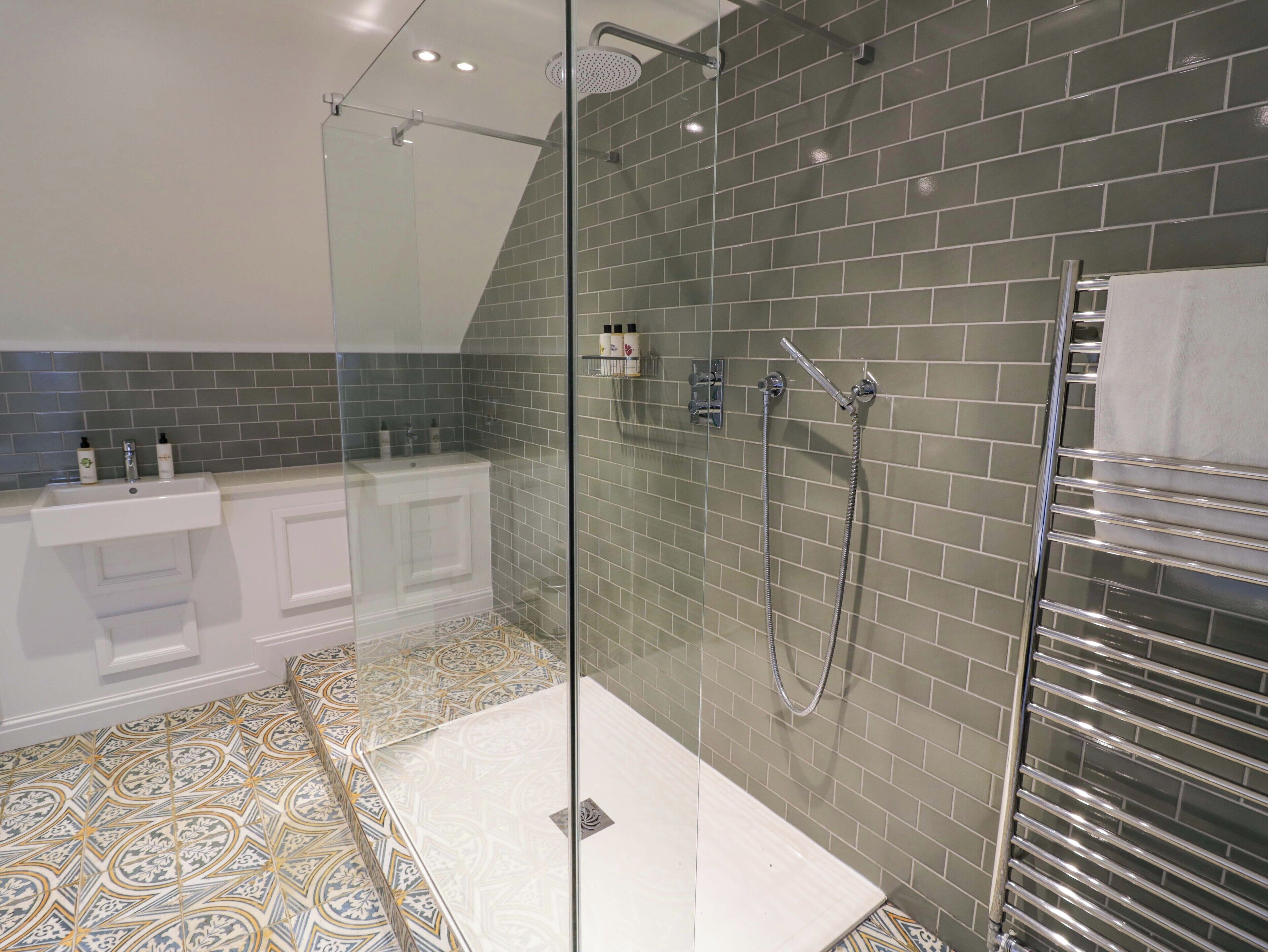 Un baño moderno con ducha de vidrio, lavamanos blanco y piso estampado.
