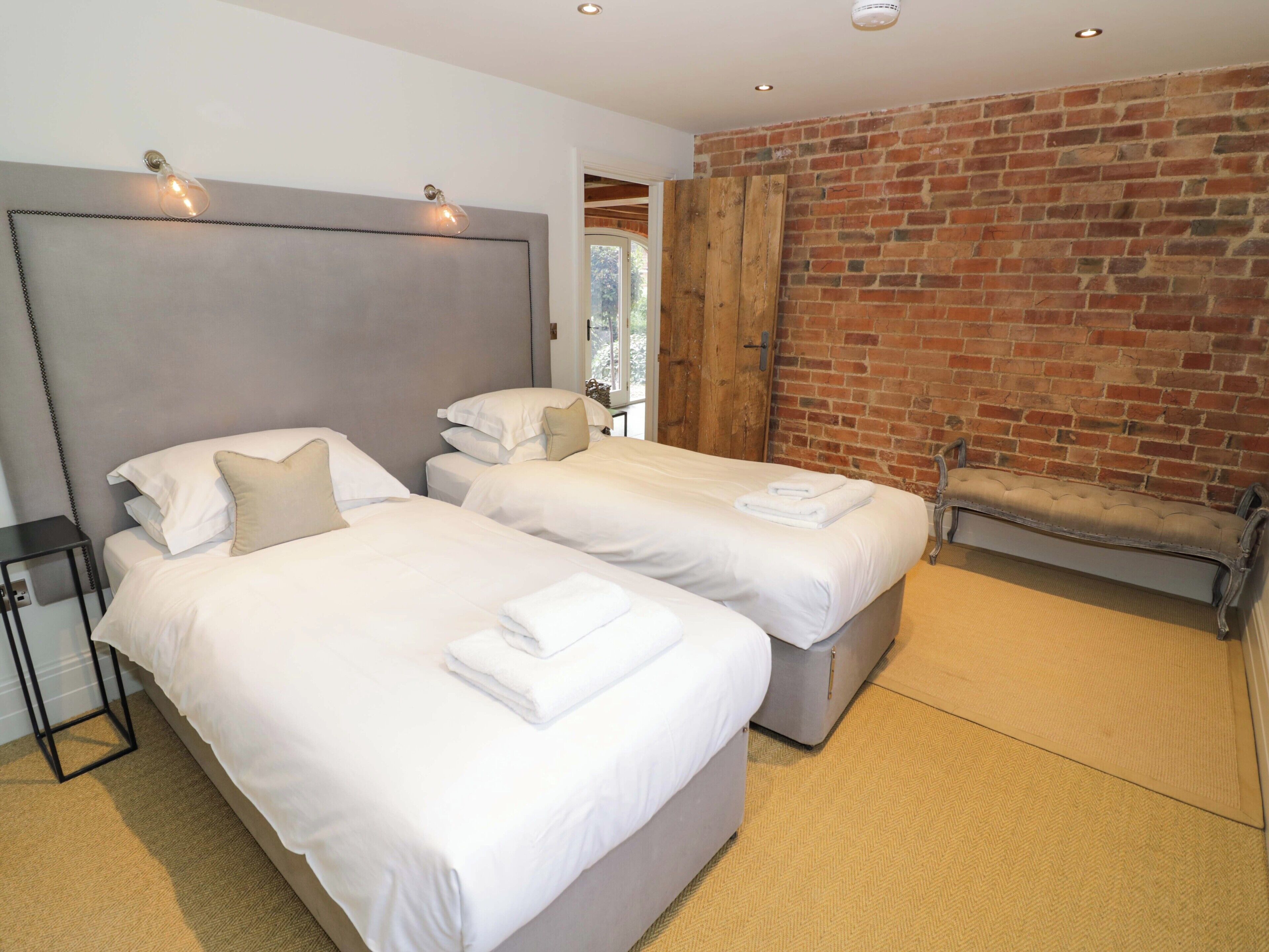 A hotel room with two beds, a brick wall, and a bench.