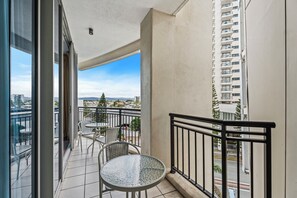 Enjoy the urban view from this balcony with a glass door, small table, and two chairs.