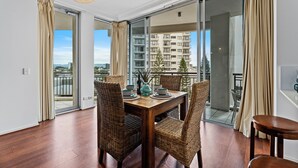 Un coin repas avec une table en bois, des chaises en osier et une vue sur un bâtiment, visible à travers des portes vitrées.