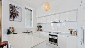 Une cuisine moderne avec des armoires blanches, un grand îlot central, des appareils en acier inoxydable et un luminaire suspendu.
