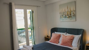 Une chambre à coucher avec un lit, des oreillers, une table de chevet, un tableau et une vue sur l’extérieur, visible à travers une porte.