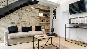 Una sala de estar moderna con una pared de piedra, un sofá con cojines negros, una mesa de centro, un televisor y una escalera.