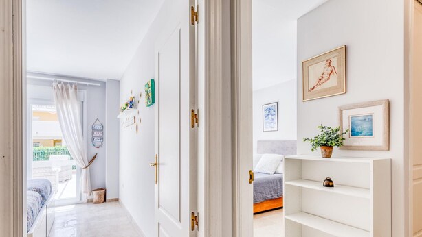 A hallway with a bed, a white shelf unit, and a door leading to another room.