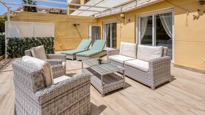 An outdoor patio with wicker furniture, a pergola, and a view of a building with balconies.
