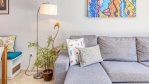 A modern living room with a grey sofa, a floor lamp, a potted plant, and a colorful abstract painting on the wall.