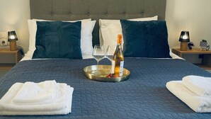 A neatly made bed with a dark blue quilt, two pillows, a tray with a bottle and glasses, and a painting of sailboats on the wall. - Stylish First Floor Two Bedroom Flat in Kassiopi with Breakfast (Κασσιόπη)