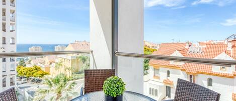 A balcony with a glass table, wicker chairs, and a potted plant.