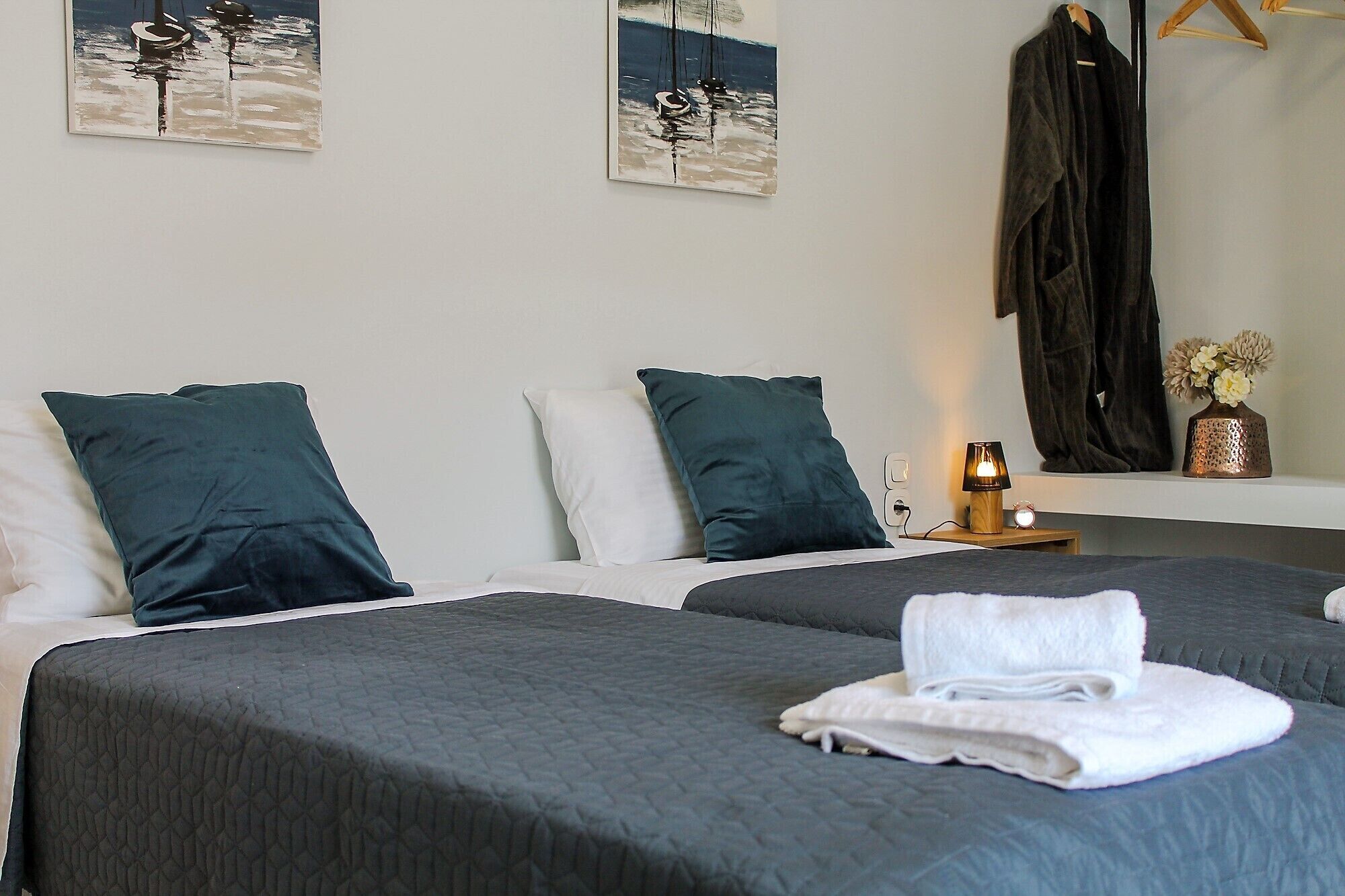 A hotel room with two beds, dark bedding, a bedside lamp, a mirror, and artwork on the wall.
