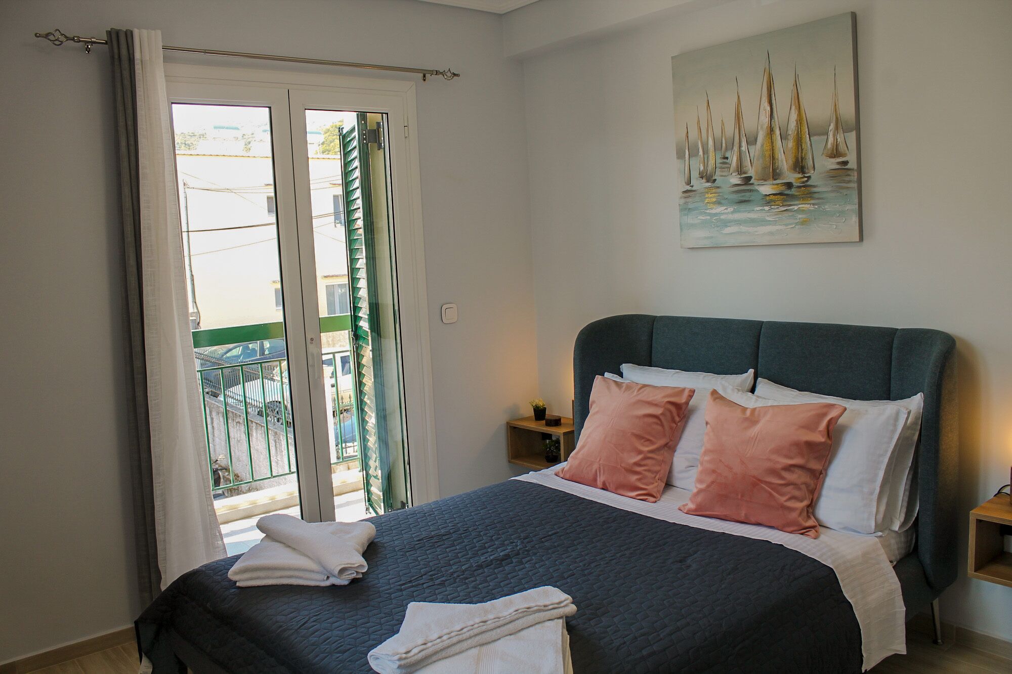 A bedroom with a bed, pillows, a nightstand, a painting, and a view through a door.