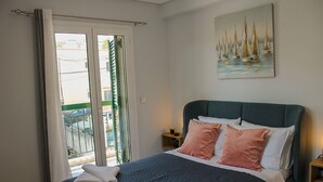 Ein Schlafzimmer mit Bett, Kissen, einem Nachttisch, einem Gemälde und Blick durch eine Tür.