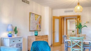 Una sala de estar con un sillón azul, una mesa de comedor con sillas, una lámpara, un cactus y un cuadro en la pared.