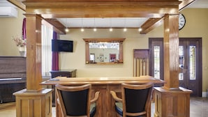 A wooden bar area with two chairs, a television, and a clock on the wall.
