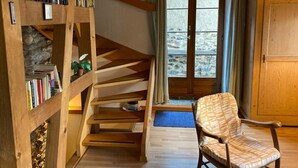 A wooden staircase leading to a balcony, a chair, and a bookshelf with books.