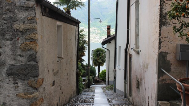 A narrow alleyway with stone walls, a tiled path, and a view of a mountainous landscape.