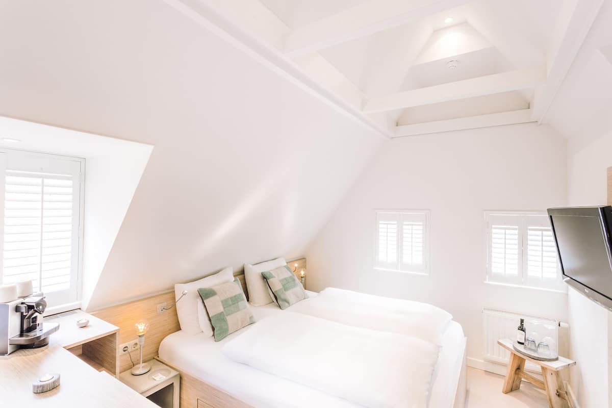 A bedroom with a bed, bedside table, lamp, and a TV mounted on the wall.