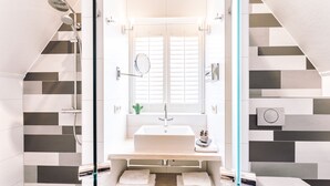 A modern bathroom with a glass shower enclosure, a white sink, and a mirror. - Logement Overzee (Nes)