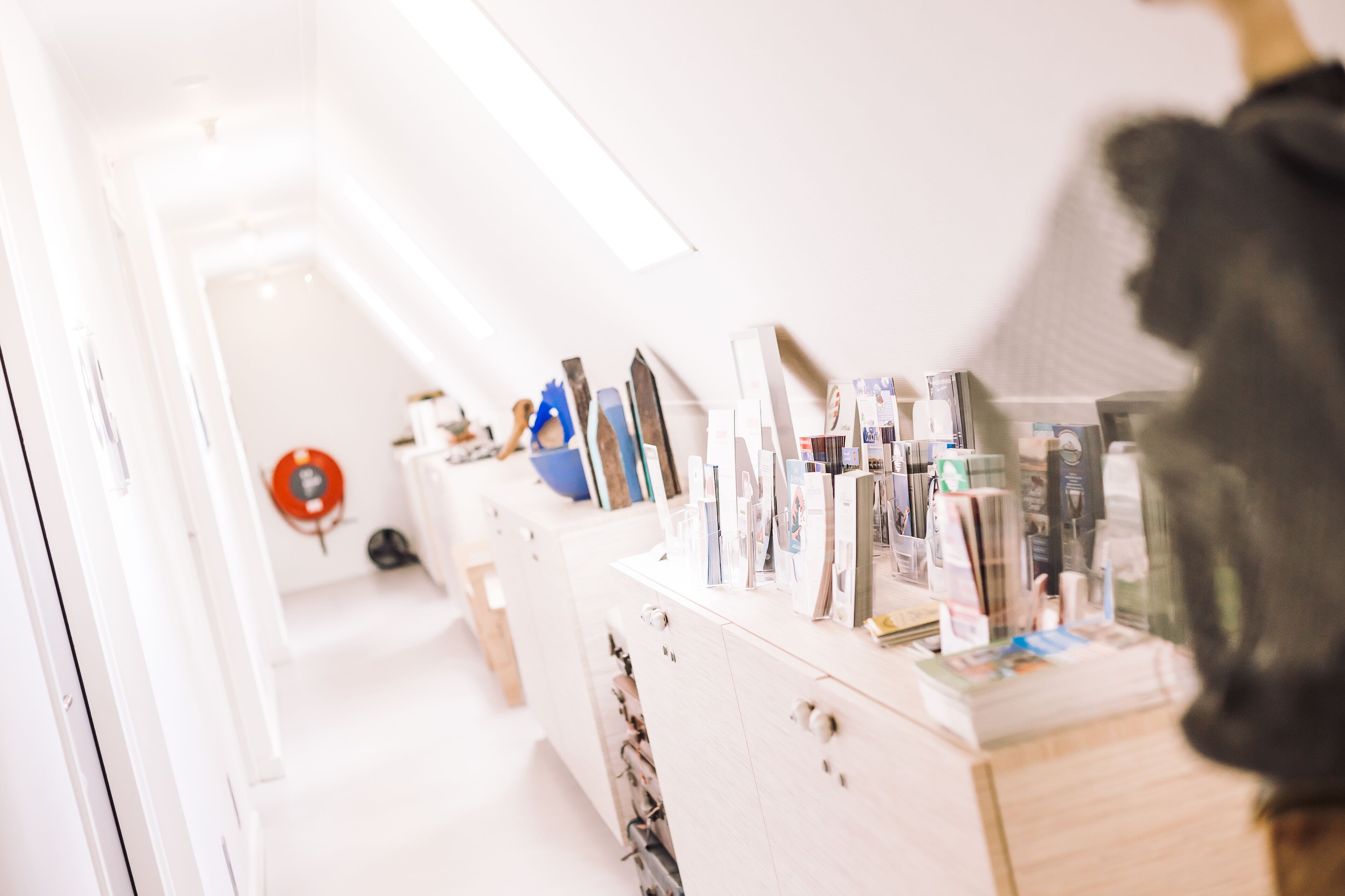 A modern, well-lit room with a white vanity and various toiletries. A red fire extinguisher is mounted on the wall.