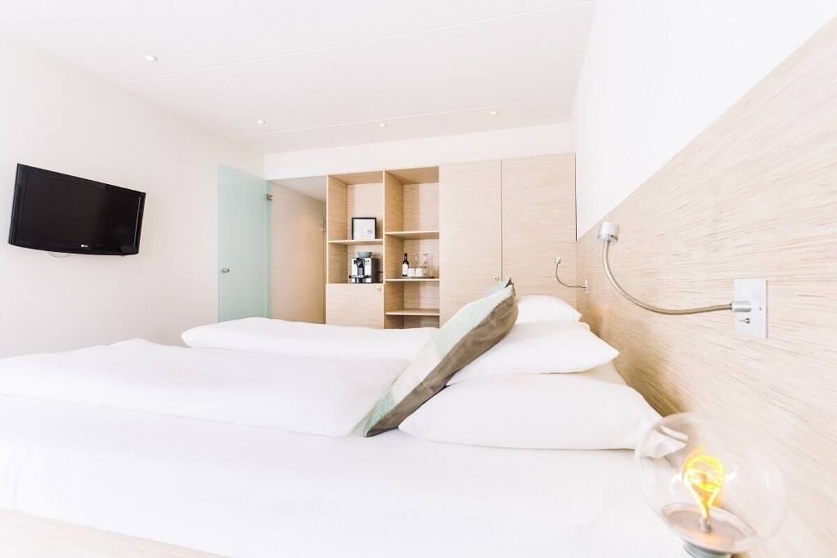 A hotel room with a bed, a television mounted on the wall, and a built-in shelf unit with various items.