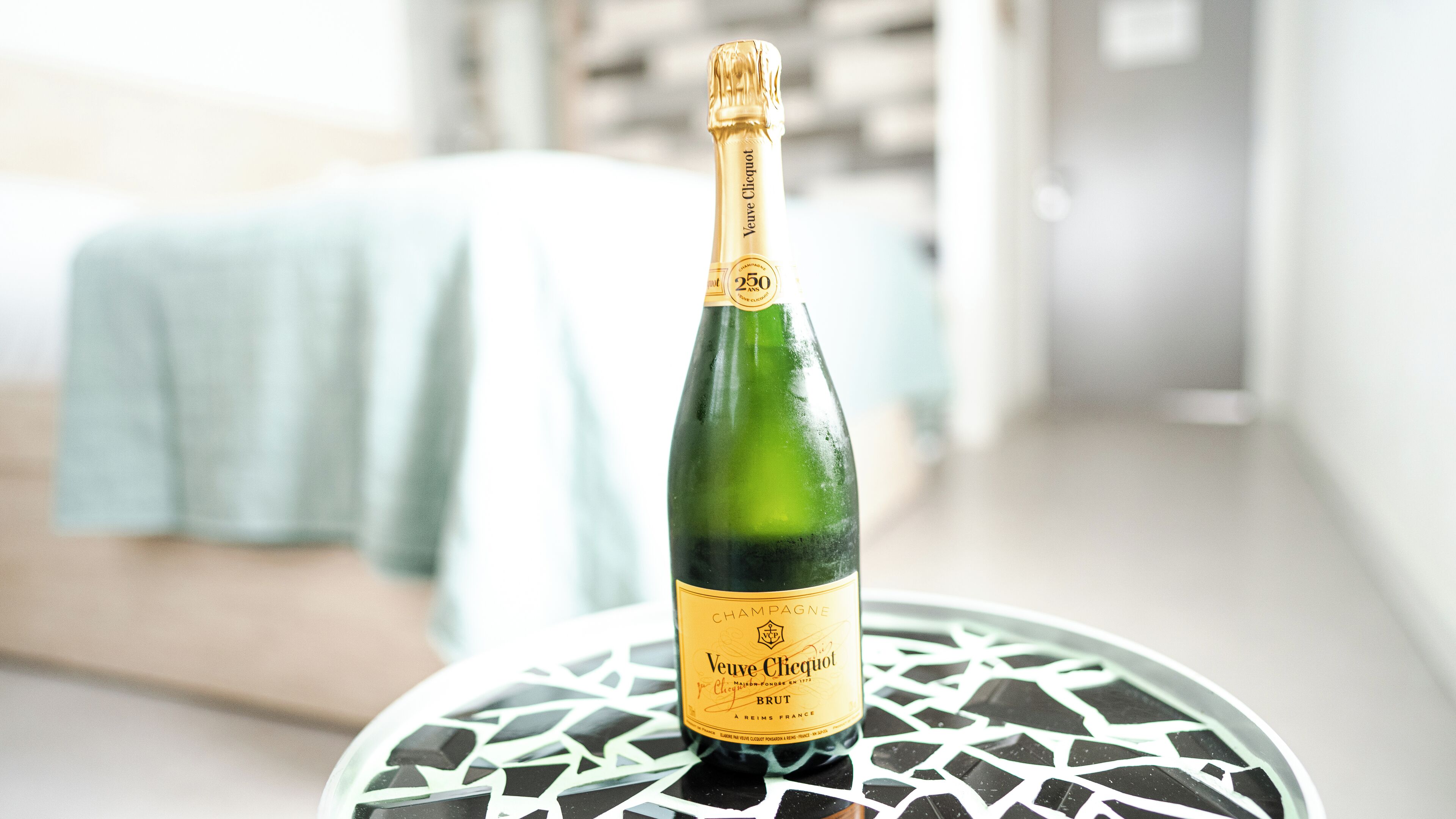 A bottle of Veuve Clicquot champagne on a glass table in a hotel room.