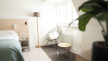 Ein Schlafzimmer mit Bett, Nachttisch, Lampe, Stuhl und einem kleinen Tisch mit einem Hut.