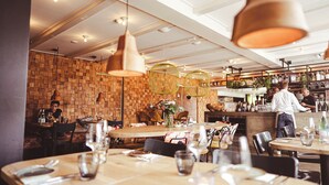 A restaurant interior with wooden walls, hanging pendant lights, and a bar area. - Logement Overzee (Nes)