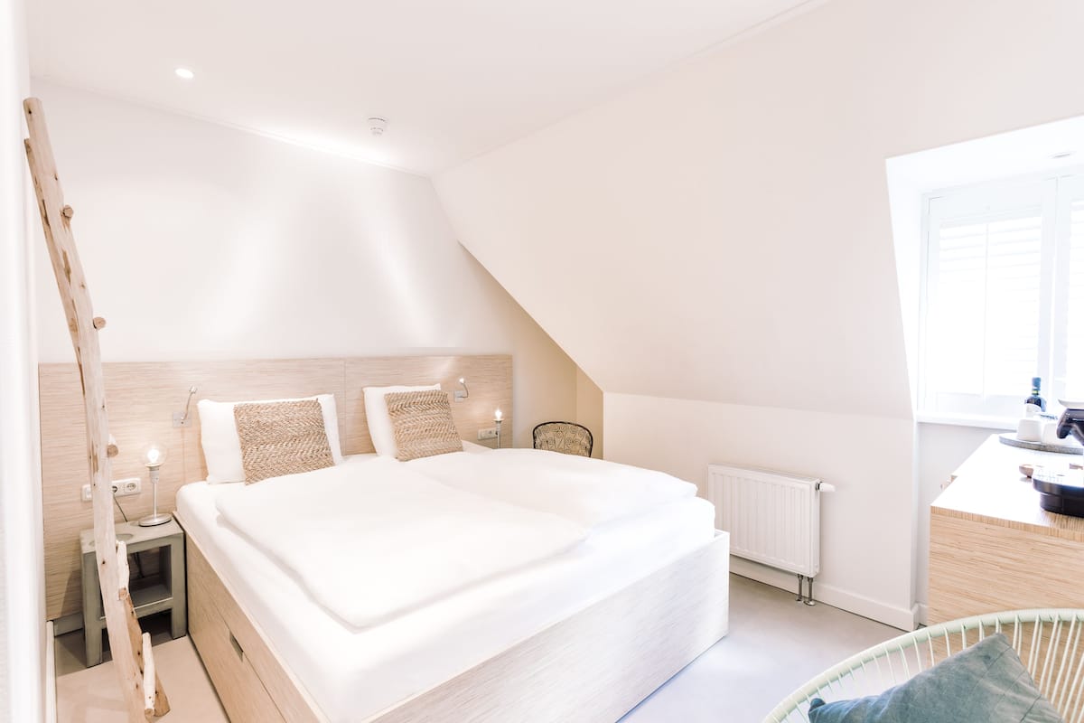 A modern bedroom with a large bed, bedside tables, a chair, and a window.