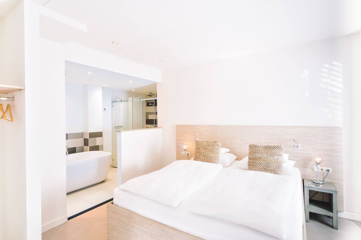 A modern hotel room with a large bed, a separate bathroom, and a small bedside table with a lamp.