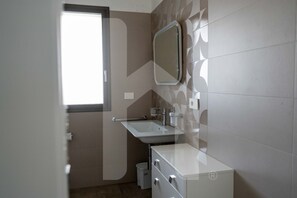 Une salle de bain avec une fenêtre, un lavabo, un miroir et un meuble de rangement.