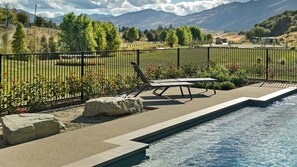 A pool area with a lounge chair and a table, surrounded by a fence and greenery. - Countryside Escape Arrowtown (Arrowtown)
