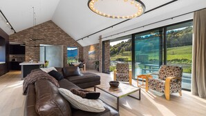 A modern living room with a large window, a brown leather sofa, and patterned chairs. - Countryside Escape Arrowtown (Arrowtown)