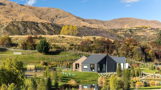 A modern house with a brick facade and a dark roof, surrounded by a well-maintained garden and a cemetery. - Countryside Escape Arrowtown (Arrowtown)