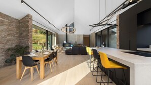 A modern kitchen with a central island, a dining area with a wooden table and chairs, and a large window offering a view of the outdoors. - Countryside Escape Arrowtown (Arrowtown)