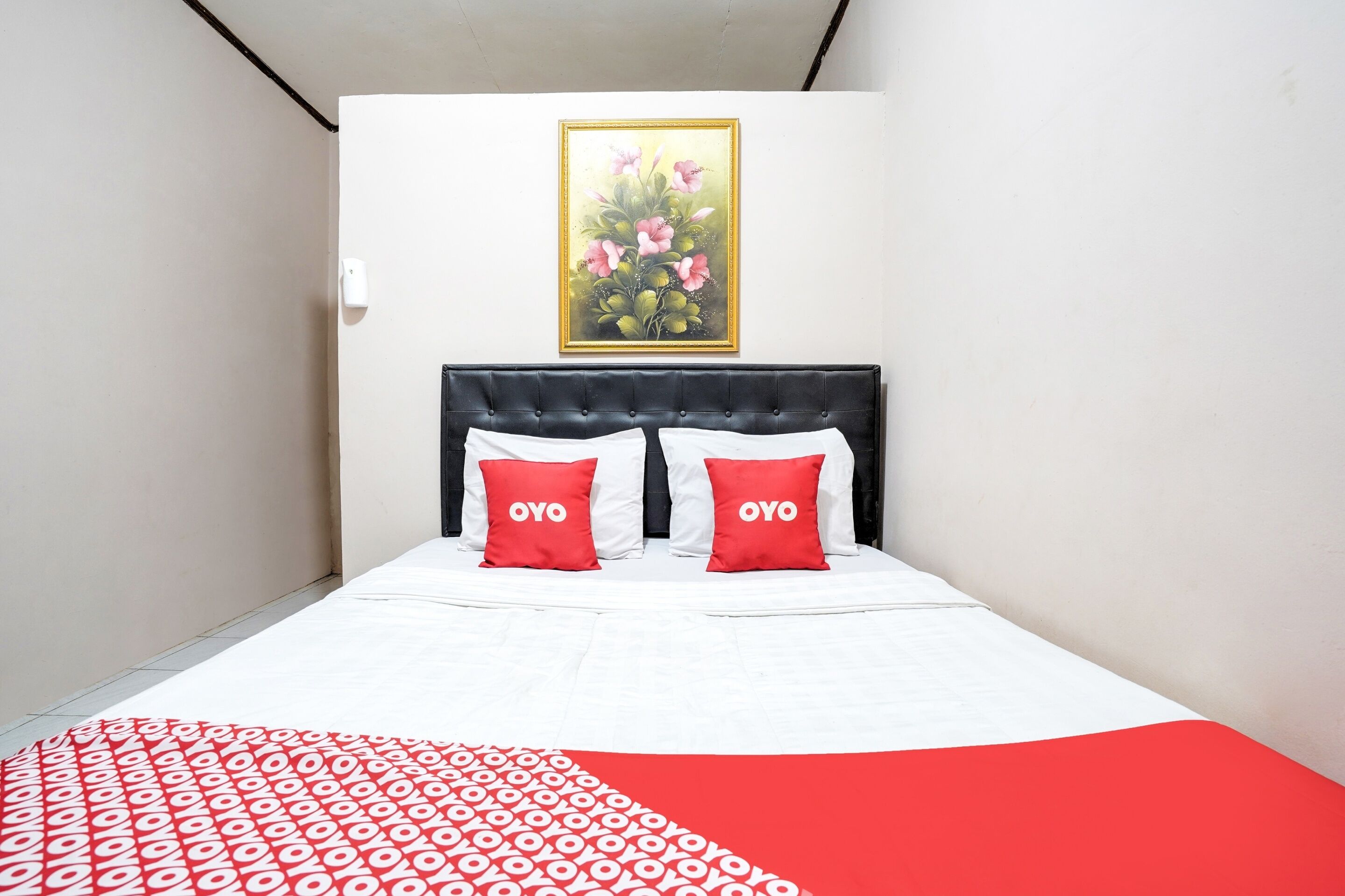 A neatly made bed with white and red bedding, a black headboard, and two red pillows with the word "OYO" on them.