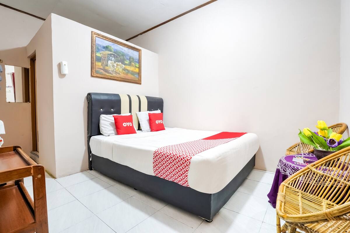 Ein ordentlich eingerichtetes Hotelzimmer mit einem Bett, einem kleinen Tisch mit Blumen und einem Korbstuhl.