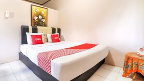 Ein Hotelzimmer mit Bett, einem kleinen Tisch mit Tischdecke, einem gerahmten Bild an der Wand und einer weißen Wand.