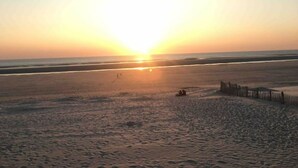 A beach with a sunset, a wooden fence, and a few people walking.