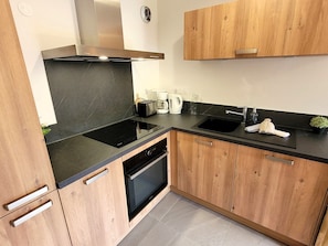 A modern kitchen with wooden cabinets, a black countertop, a built-in oven, and a stainless steel range hood.