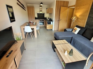A modern living space with a sofa, coffee table, TV, kitchen area, and dining table.