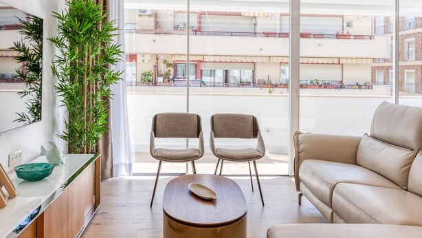 Un salon moderne comprenant un canapé, deux fauteuils, une table basse et une grande fenêtre donnant sur un quartier résidentiel.