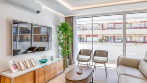 Un salon moderne doté d’une grande fenêtre, d’un canapé, de deux fauteuils, d’une table basse, d’une plante et d’un mur miroitant.