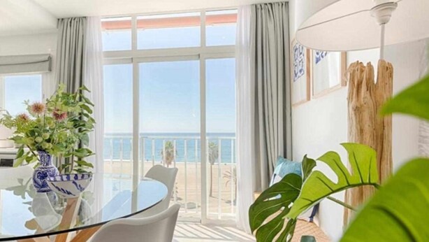 Ett modernt matområde med ett glasbord, vita stolar och utsikt över havet.