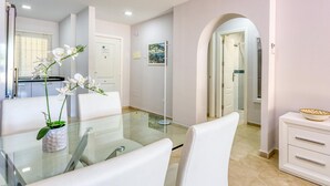 Un comedor moderno con una mesa de vidrio, sillas blancas y una orquídea en maceta.
